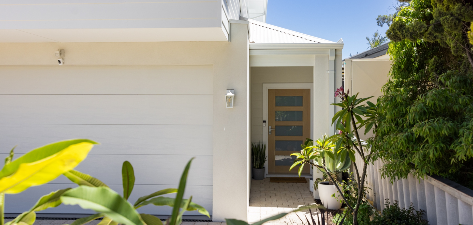 Modern home entrance with plants and clear sky.